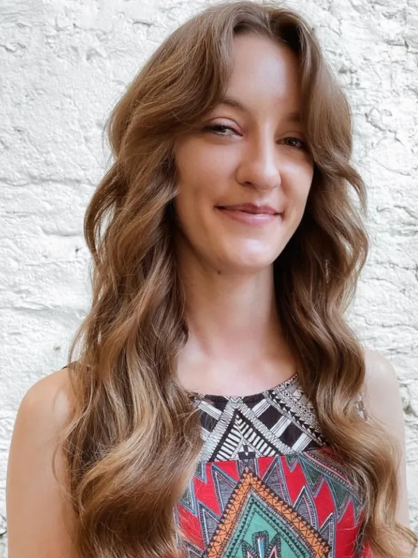 A professional portrait of Karee Garvin smiling, wearing a colorful geometric-patterned top against a white brick wall.